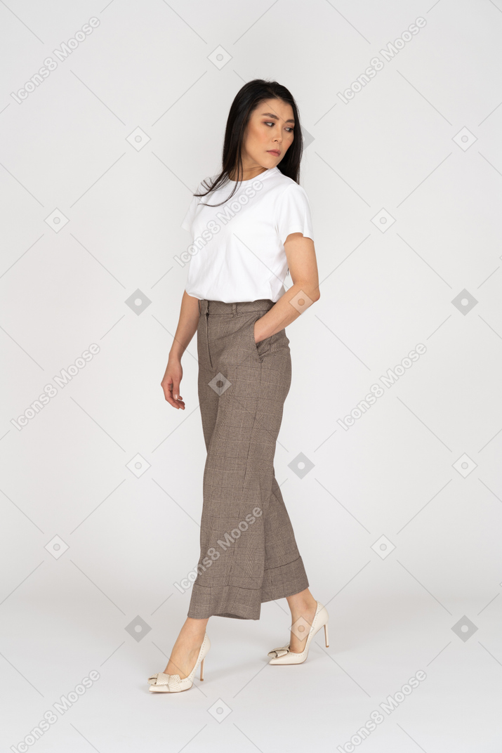 Vista di tre quarti di una giovane donna che cammina in calzoni e t-shirt che osserva da parte