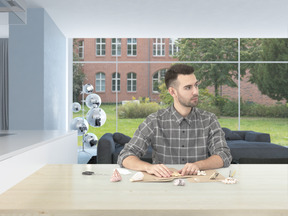 Handsome young man in a checkered shirt, sitting in a bright modern room crafting something from craft paper and seashells