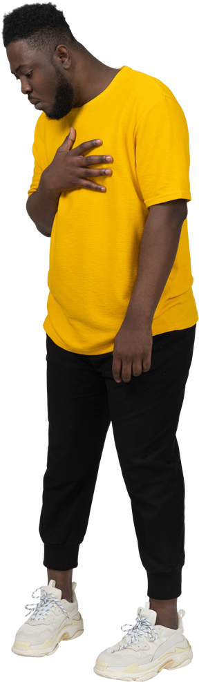 가슴을 만지는 노란색 티셔츠를 입은 검은 피부를 가진 놀란 젊은 남자의 4분의 3 보기