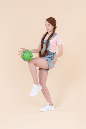 Teenage girl kicking ball by the knee