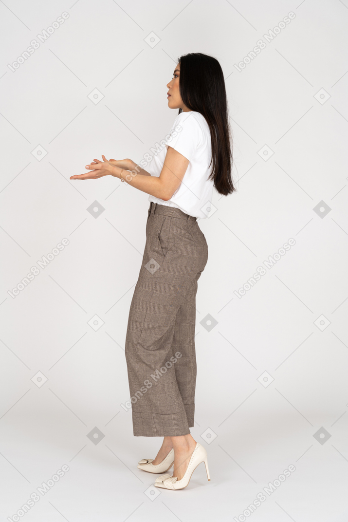 Side view of a questioning young lady in breeches and t-shirt raising hands