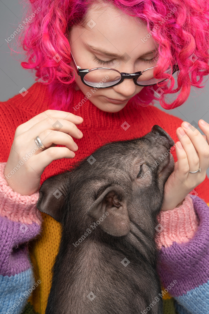 Une femme aux cheveux roses caresse un petit cochon heureux