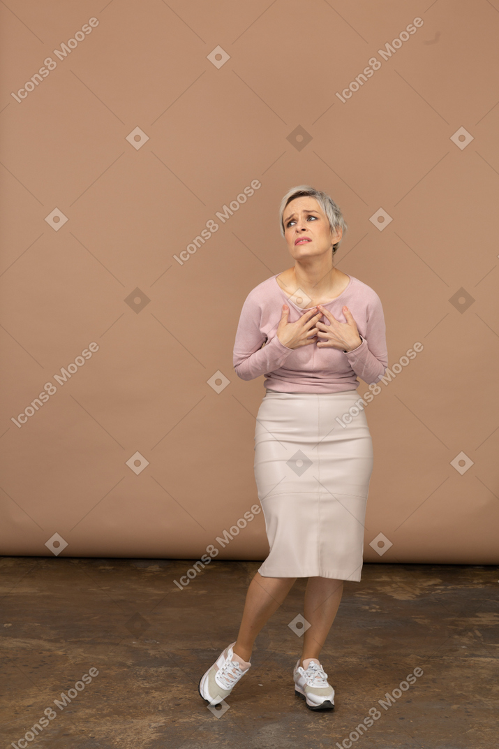 胸に手を置いて立って見上げるカジュアルな服装の感情的な女性の正面図
