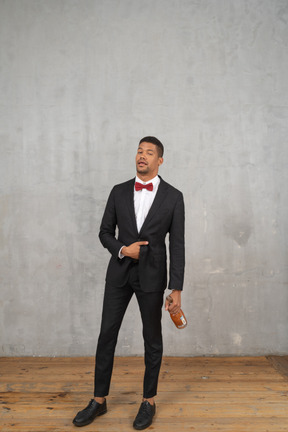 Intoxicated man in suit and bow tie holding a bottle