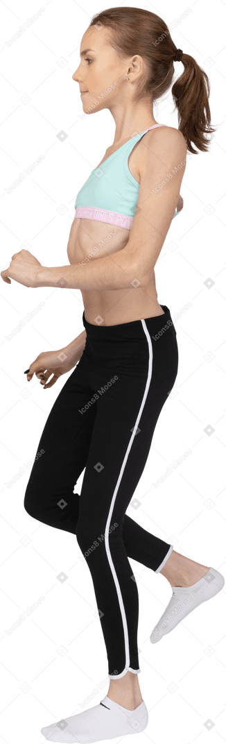 Side view of a teen girl in sportswear tilting shoulders raising leg