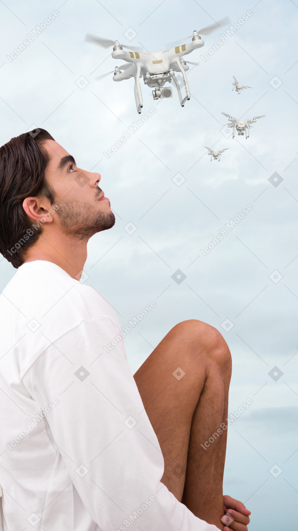 A man sitting on the ground looking up at a flying drone
