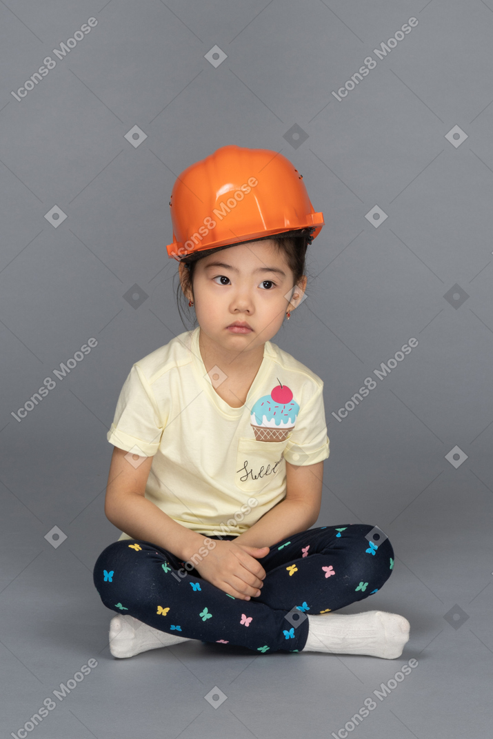 Full length portrait of a little girl looking pensive while wearing a hard hat