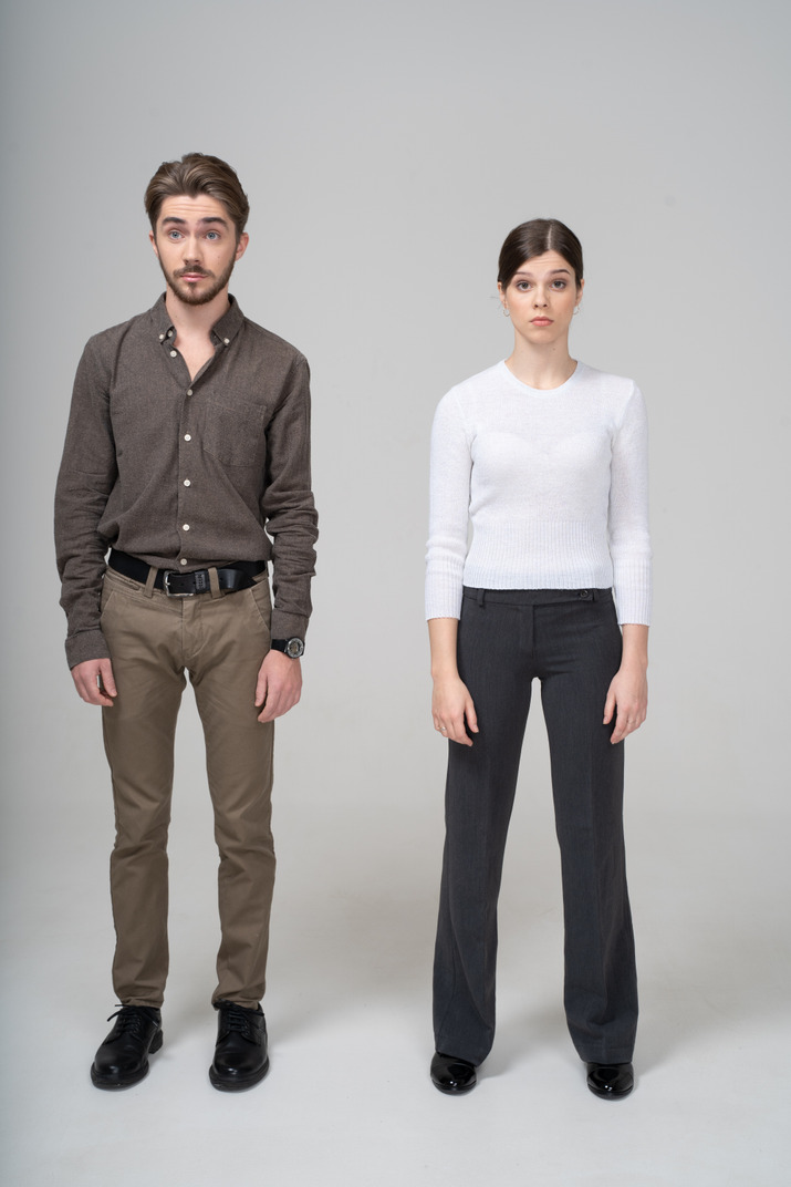 Front view of a surprised young couple in office clothing raising brows