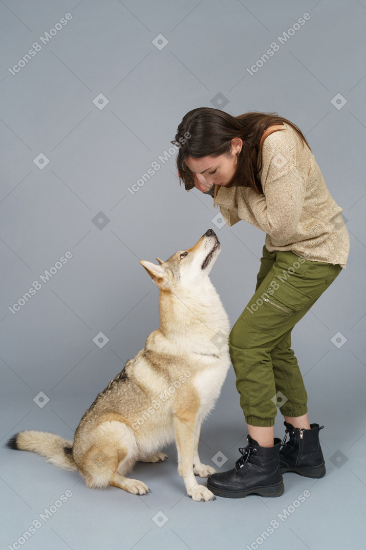 A figura intera di una giovane femmina chinandosi sul suo cane e guardando in basso