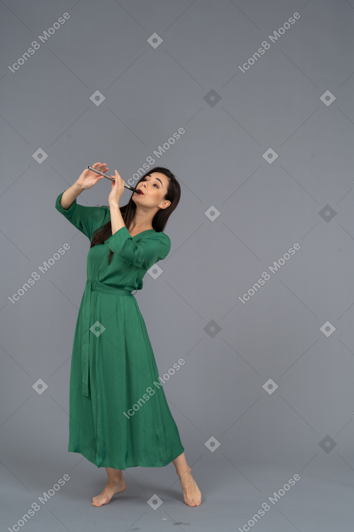 Vista de três quartos de uma jovem de vestido verde tocando flauta enquanto se inclina para trás