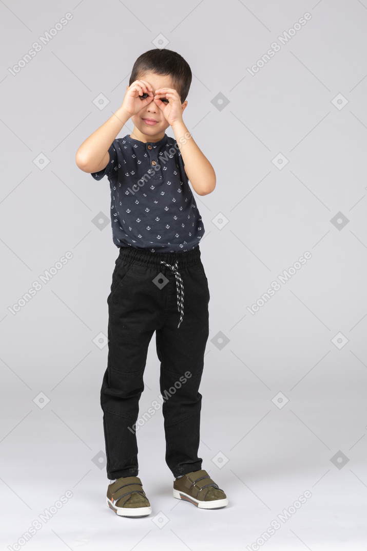 Vista frontal de um menino bonito em roupas casuais olhando por entre os dedos
