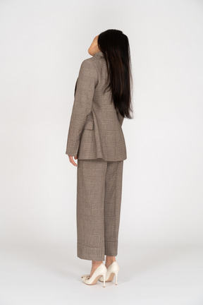 茶色のビジネススーツの傾いた頭の若い女性の4分の3の背面図