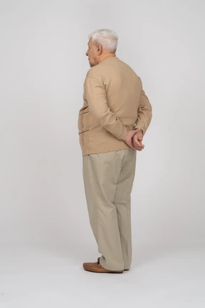 Rear view of an old man in casual clothes standing with hands behind back