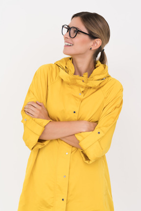 Mulher de capa de chuva amarela e óculos com as mãos postas, olhando de lado