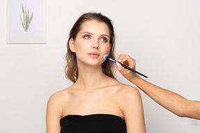 Vista frontal de un maquillador aplicando polvos faciales para un modelo femenino