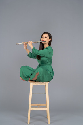 Full-length of a young lady playing the clarinet sitting with her legs crossed on a wooden chair