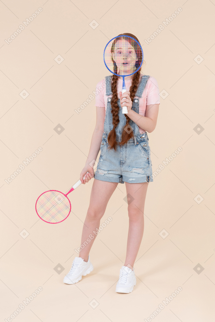 Teenage girl holding racket in one hand and closing a face with another one