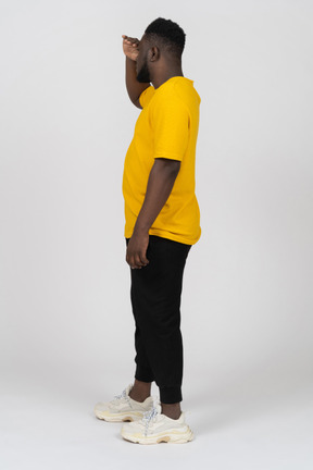 Vista laterale di un giovane uomo dalla pelle scura in maglietta gialla che cerca qualcosa