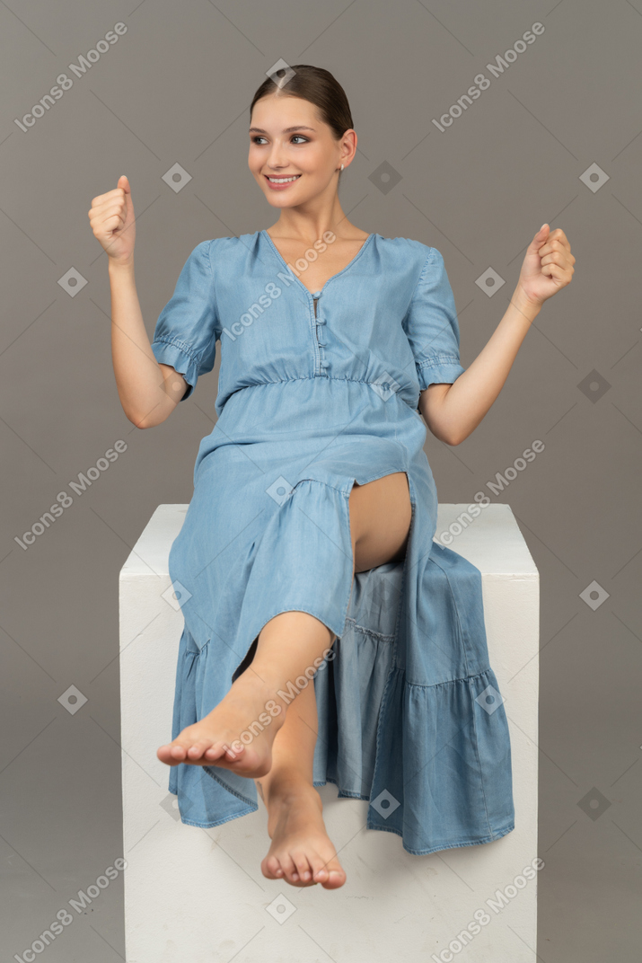 Вид спереди веселой молодой женщины, сидящей на кубе и улыбающейся