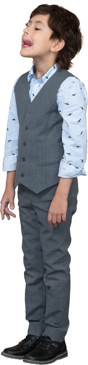Вид сбоку симпатичного мальчика в сером костюме, показывающего язык