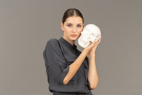 Front view of a young woman in a jumpsuit holding a plaster skull