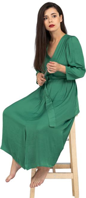 A figura intera di una giovane donna in abito verde, seduta su una sedia mentre si tiene il clarinetto
