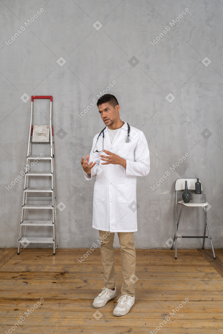 はしごと椅子のある部屋に立っている若い身振りで示す医師の4分の3のビュー