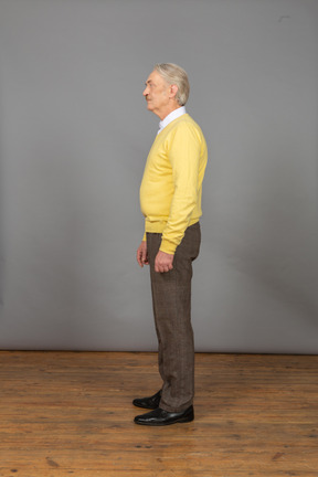 Vista lateral de um velho vestindo um pulôver amarelo e parado