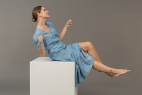 Вид сбоку на молодую женщину, сидящую на кубе и пытающуюся сохранить равновесие
