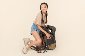 Junger asiatischer weiblicher reisender, der nahe sehr großem touristischem rucksack sitzt