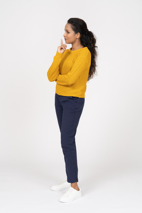Vista lateral de una chica pensativa en ropa casual apuntando hacia arriba con un dedo