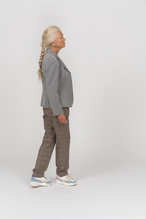 Vista laterale di una vecchia signora in abito in piedi con le gambe incrociate