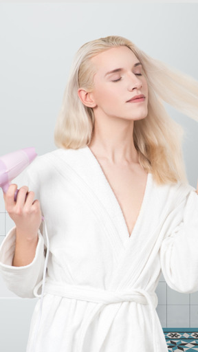 A woman in a bathrobe is drying her hair with a hair dryer