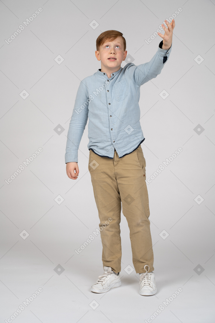 Front view of a boy standing with raised arm and looking up