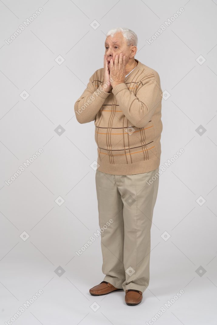 Front view of an impressed old man in casual clothes covering mouth with hands