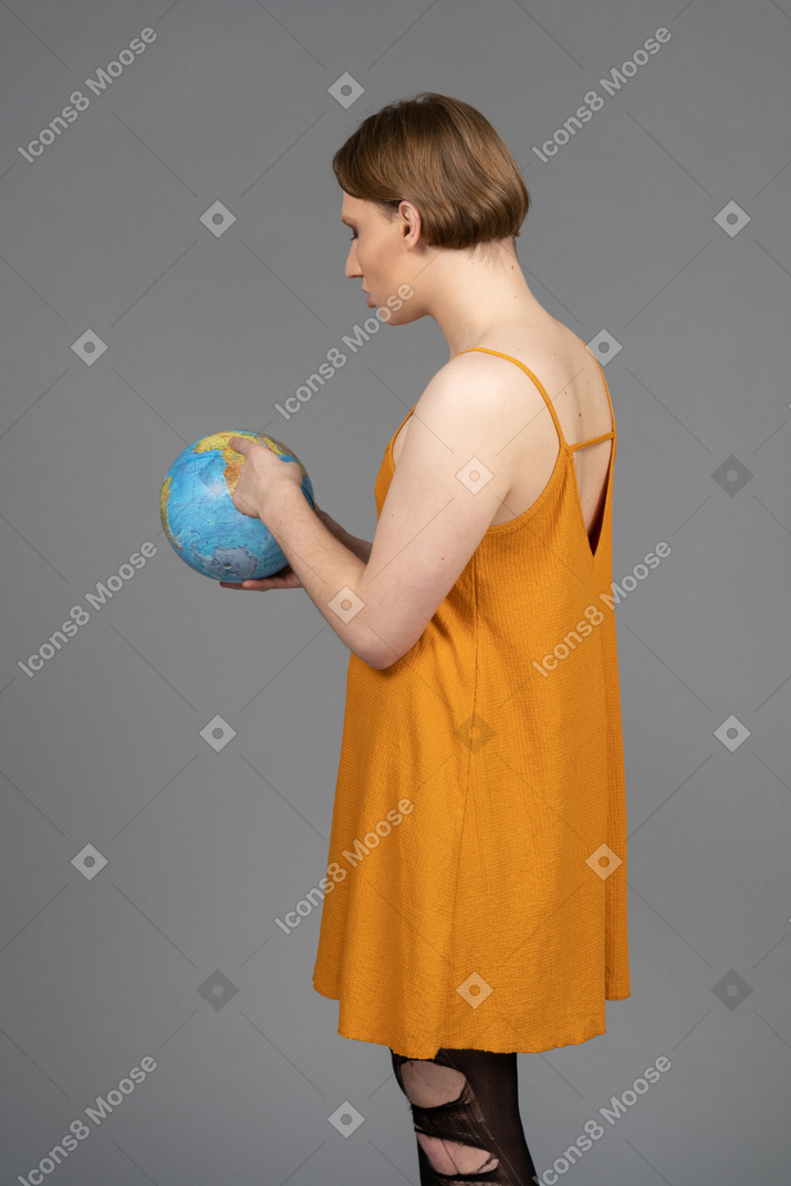 地球上のどこかを指している若いトランスジェンダーの人の背面図