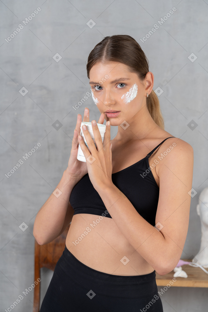 Attraente giovane donna che tiene crema per il viso