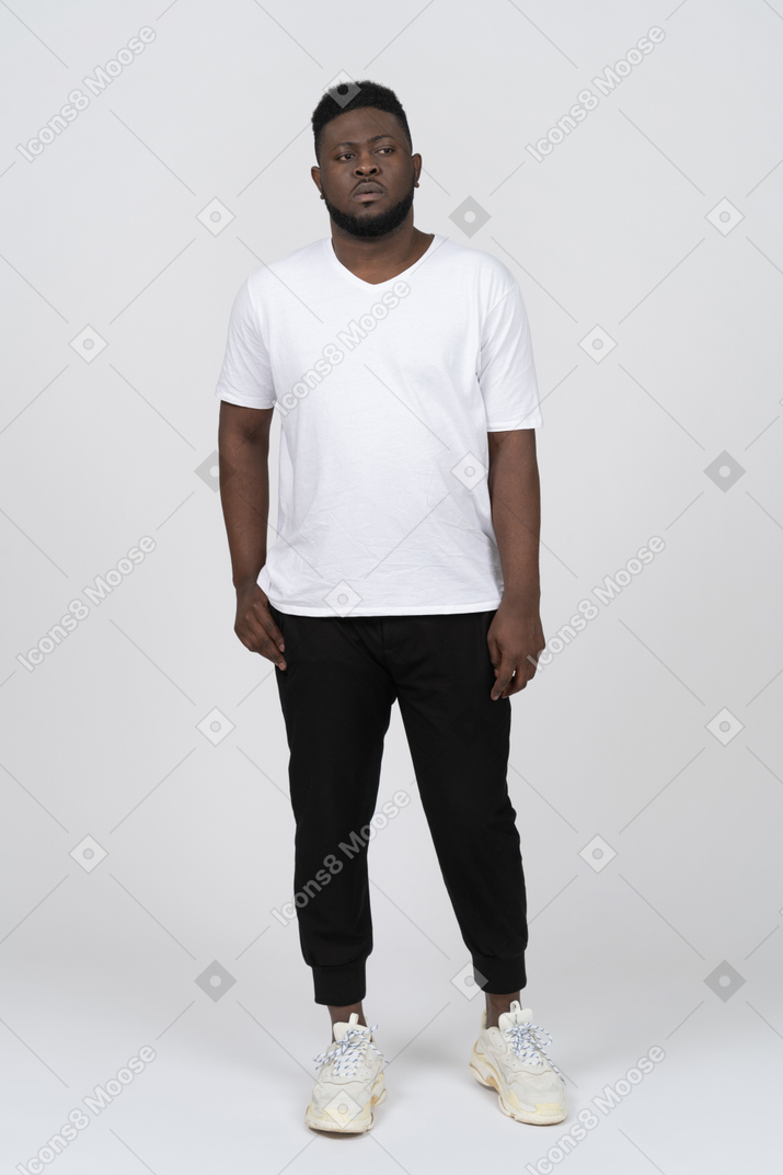 흰색 티셔츠를 입은 짙은 색의 젊은 남자가 가만히 서 있는 모습