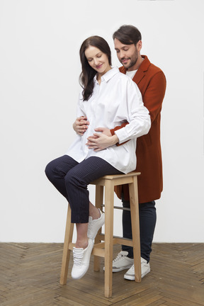 Mann umarmt sitzende schwangere frau von hinten