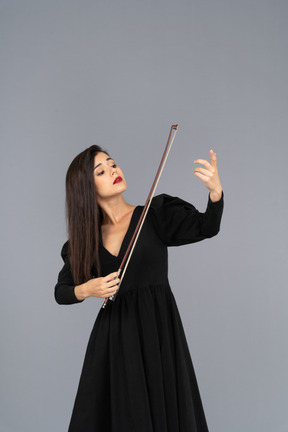 Вид спереди молодой дамы в черном платье, производящей впечатление игры на скрипке