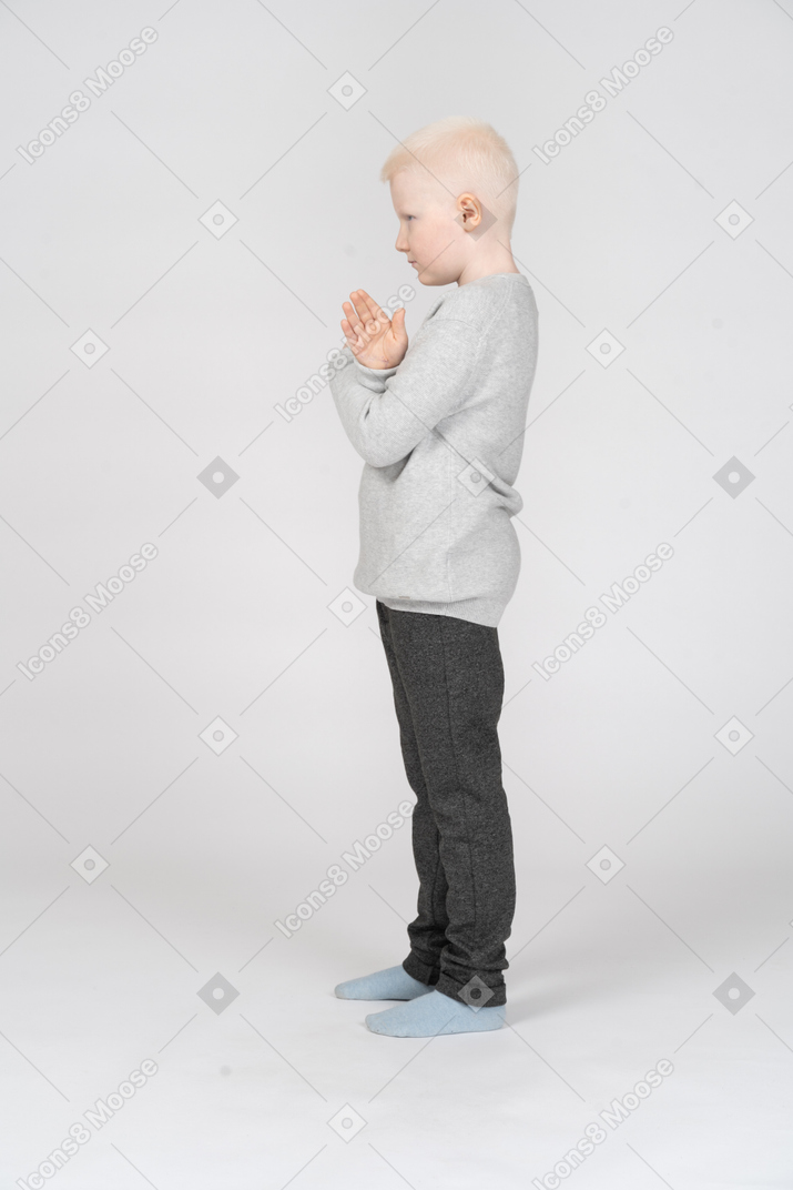 Vista lateral de un niño pequeño con las manos cruzadas