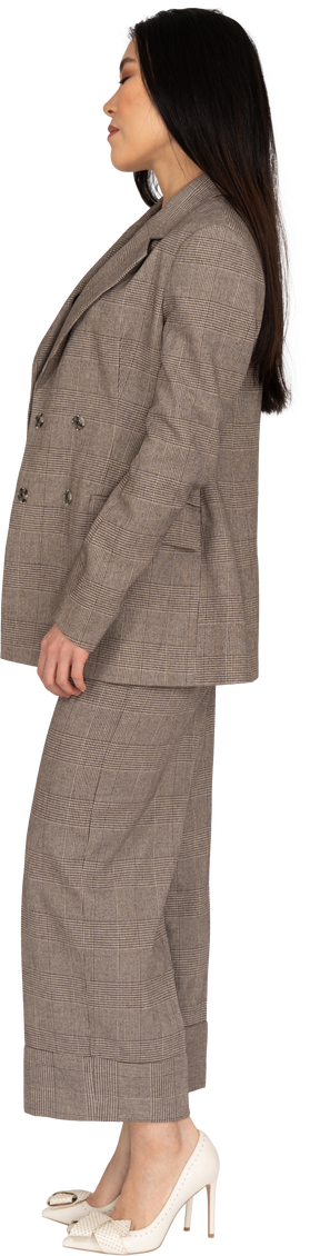 Side view of a young lady in brown business suit standing with her eyes closed