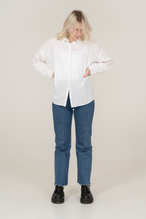 Front view of a blonde female in casual clothes putting hands on hips and looking down