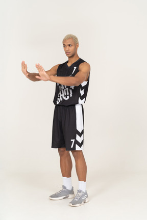 Vista di tre quarti di un giovane giocatore di basket maschile che si rifiuta di allungare le braccia