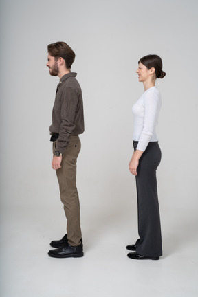 Vista lateral de una joven pareja disgustada haciendo muecas en ropa de oficina