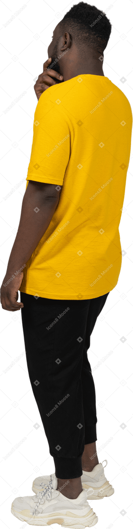 あごに触れている黄色のtシャツを着た推測の若い浅黒い肌の男の4分の3の背面図