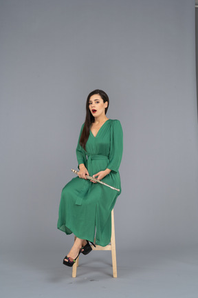 Три четверти удивленной барышни в зеленом платье сидят на стуле с кларнетом