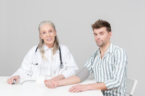 Doctora de edad revisando la presión sanguínea de un joven