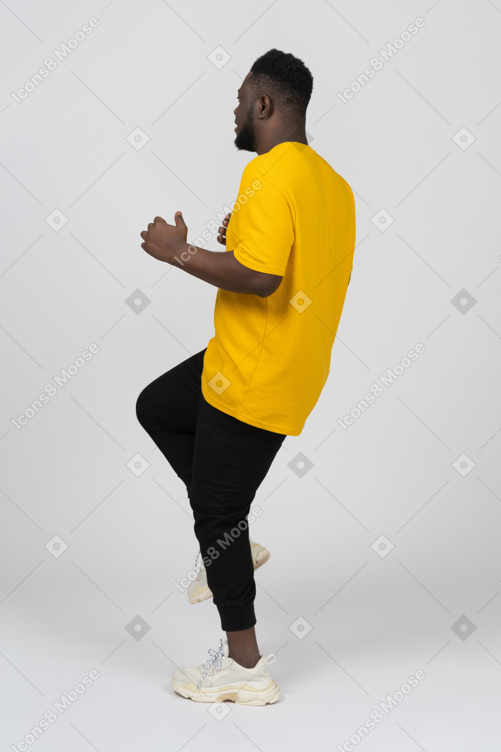 Side view of a young dark-skinned man in yellow t-shirt raising leg