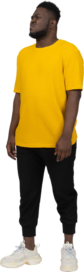 Three-quarter view of a displeased grimacing young dark-skinned man in yellow t-shirt